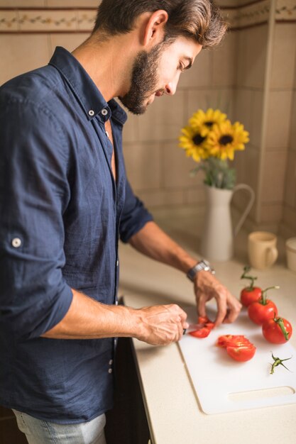 Jeune homme coupe une tranche de tomates sur une planche à découper blanche