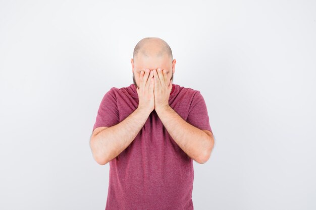 Jeune homme couvrant le visage avec les mains en t-shirt rose, vue de face.