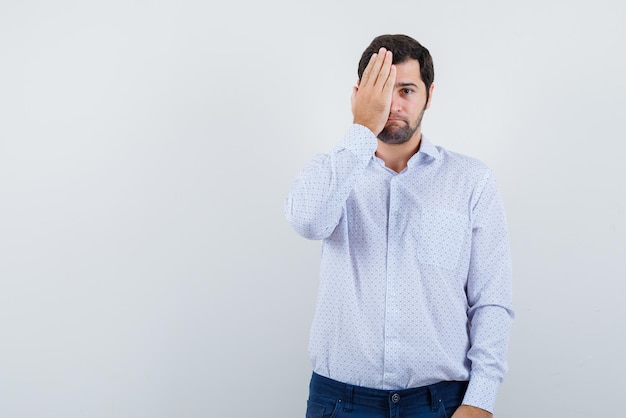 Le jeune homme couvre la moitié du visage avec la main sur fond blanc