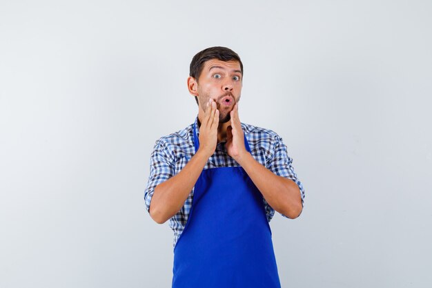 Jeune homme cuisinier dans un tablier bleu et une chemise