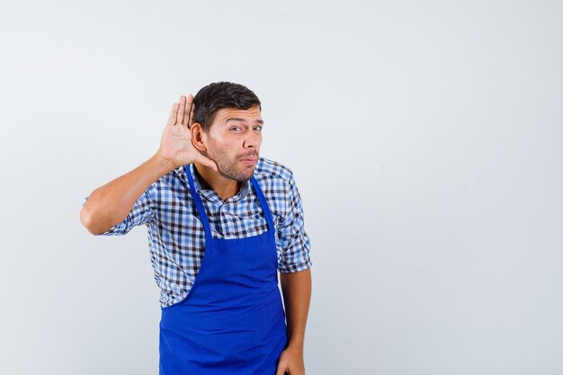 Jeune homme cuisinier dans un tablier bleu et une chemise