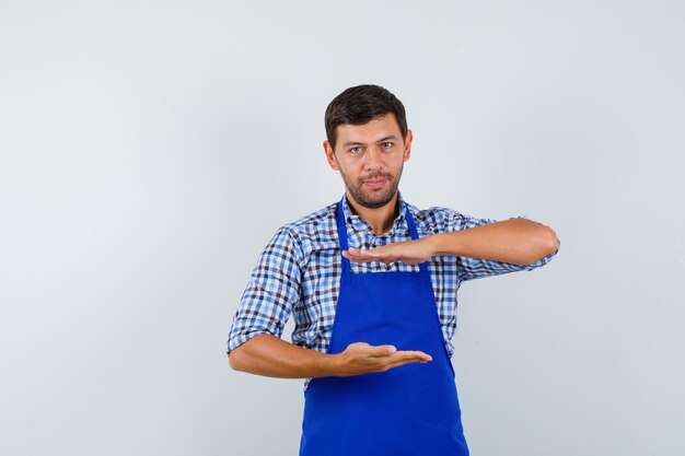 Jeune homme cuisinier dans un tablier bleu et une chemise