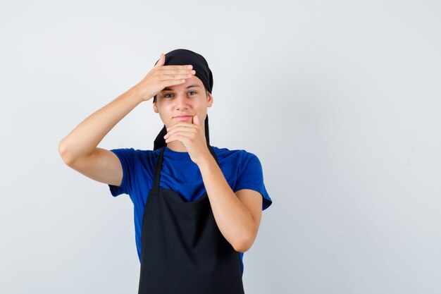 Jeune homme cuisinier faisant un geste de cadre en t-shirt, tablier et regardant mignon, vue de face.