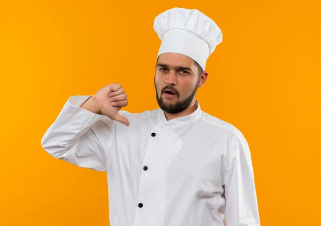 Jeune homme cuisinier impressionné en uniforme de chef pointant sur lui-même isolé sur un mur orange