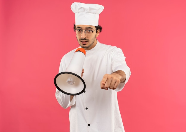 jeune homme cuisinier portant l'uniforme de chef et des lunettes parle sur haut-parleur et vous montre le geste