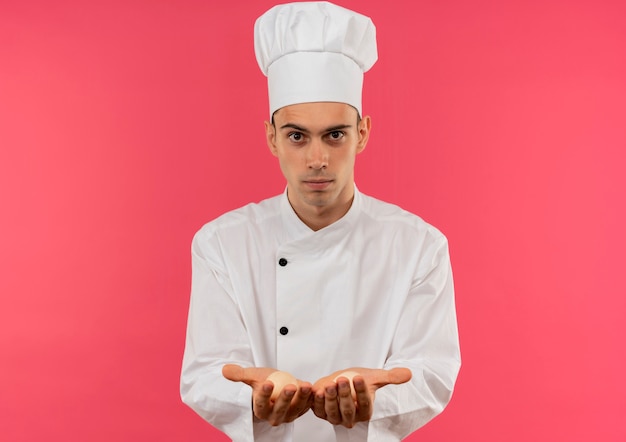 Jeune homme cuisinier portant l'uniforme de chef tenant des oeufs sur un mur rose isolé