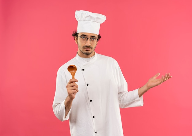 Jeune homme cuisinier portant l'uniforme de chef et des verres tenant une cuillère et répandre la main