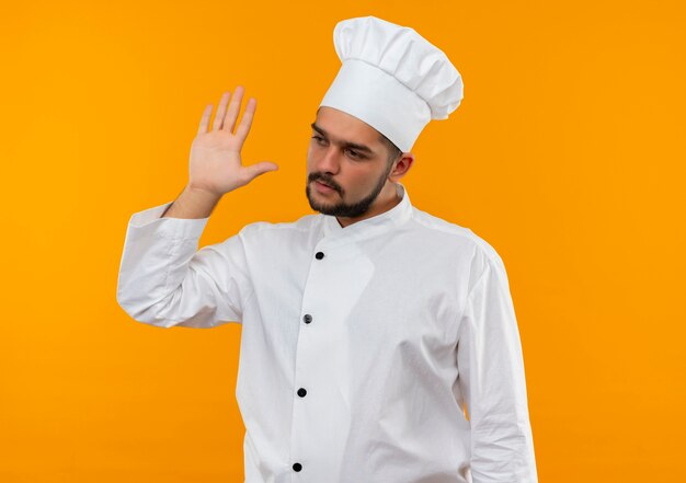 Jeune homme cuisinier en uniforme de chef regardant côté et levant la main