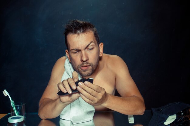 Le jeune homme dans la chambre assis devant le miroir se gratte la barbe à la maison. Concept d'émotions humaines