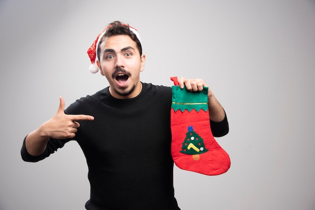 Un jeune homme dans un chapeau du Père Noël montrant une chaussette de Noël.