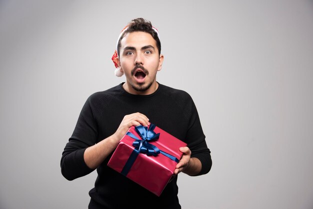 Un jeune homme dans un chapeau de père Noël tenant un cadeau du nouvel an.