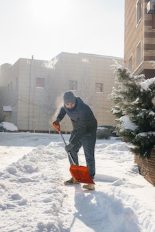Un jeune homme déblaye la neige devant la maison par une journée ensoleillée et glaciale. nettoyer la rue de la neige.