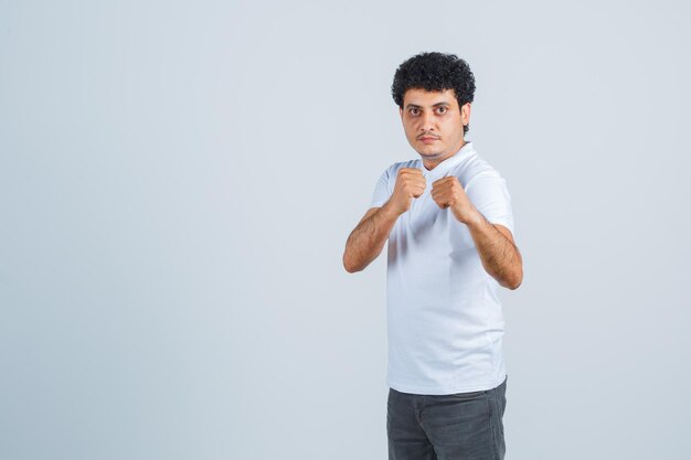 Jeune homme debout en boxer pose en t-shirt blanc et jeans et à la recherche de sérieux. vue de face.