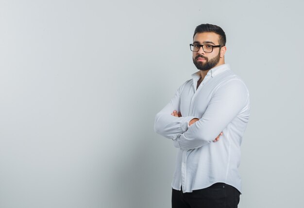 Jeune homme debout avec les bras croisés en chemise blanche, pantalon et à l'élégant