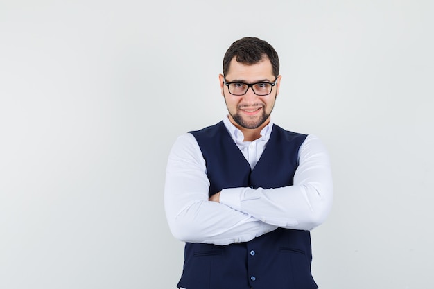 Photo gratuite jeune homme debout avec les bras croisés en chemise et gilet et à la joyeuse