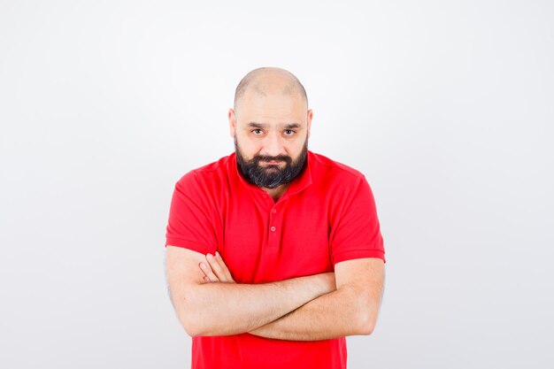 Jeune homme debout avec les bras croisés en chemise rouge et l'air calme. vue de face.