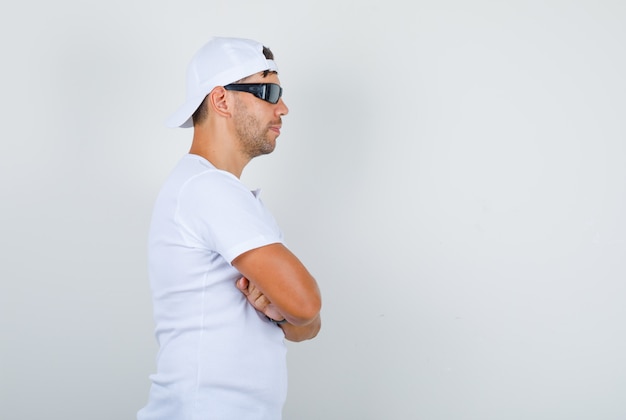 Jeune homme debout avec les bras croisés en t-shirt blanc, casquette, lunettes et à la confiance. .