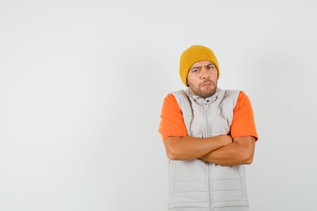 Jeune homme debout avec les bras croisés en t-shirt, veste, chapeau et à la stricte