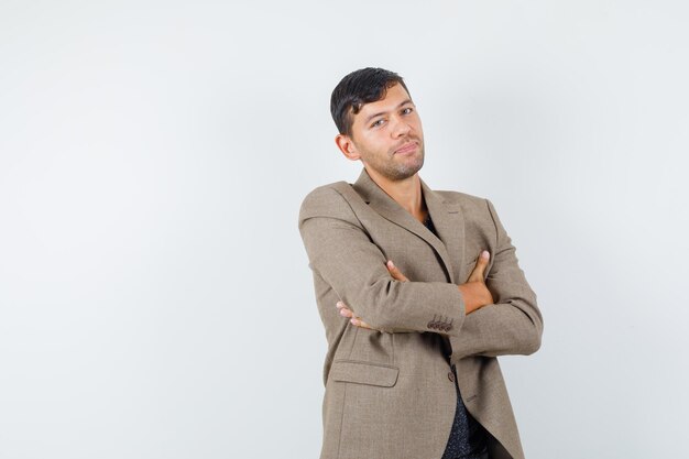 Jeune homme debout avec les bras croisés en veste marron grisâtre, chemise noire et l'air calme. vue de face. espace libre pour votre texte