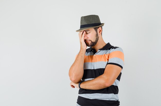 Jeune homme debout dans la pensée pose en t-shirt, chapeau et à la recherche d'épuisé.