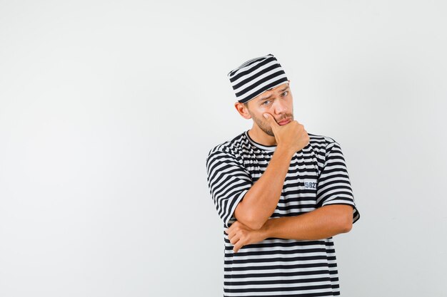 Jeune homme debout dans la pensée pose en t-shirt rayé, chapeau et à la recherche sensible.