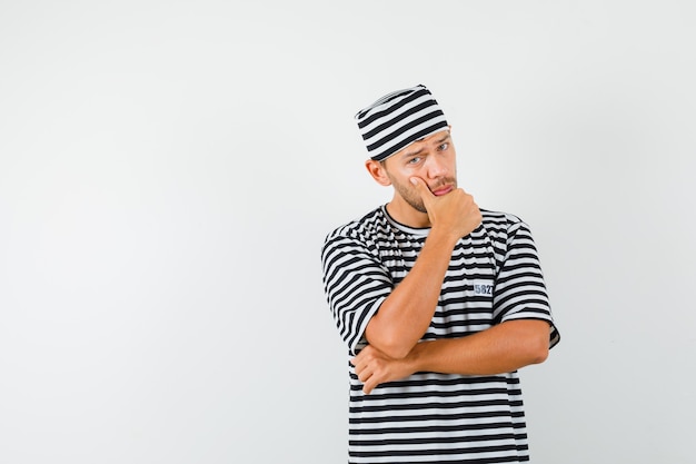 Jeune homme debout dans la pensée pose en t-shirt rayé, chapeau et à la recherche sensible.