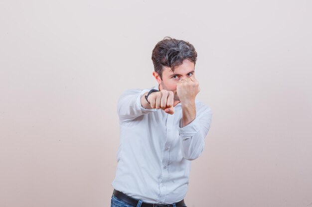 Jeune homme debout dans la pose de combat en chemise blanche, jeans et à fort