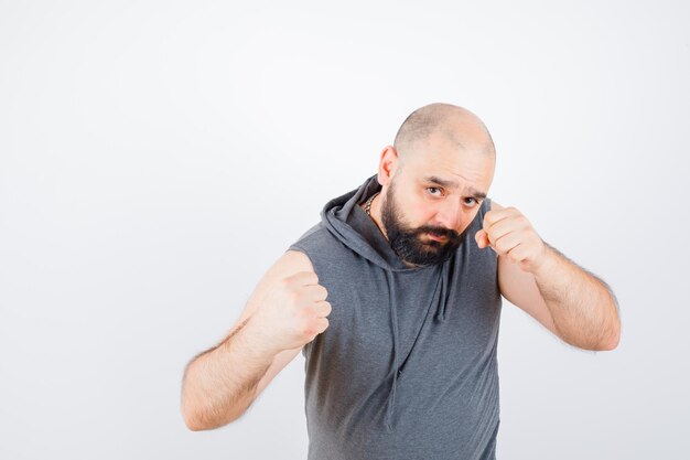 Jeune homme debout dans la pose de combat en sweat à capuche sans manches et l'air confiant. vue de face.