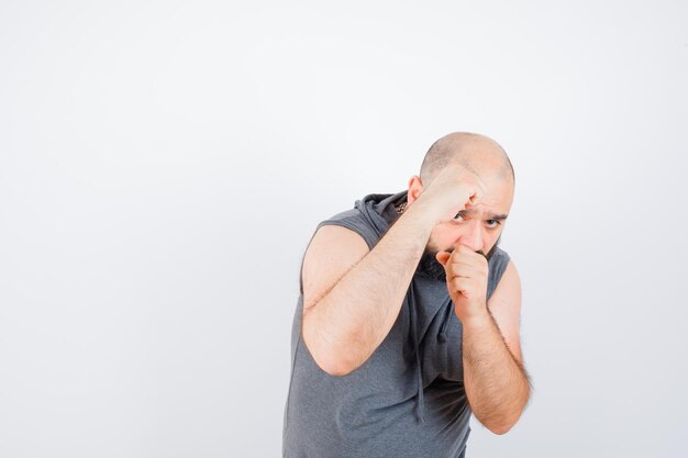 Jeune homme debout dans la pose de combat en sweat à capuche sans manches et l'air confiant. vue de face.