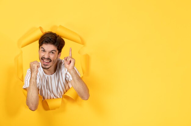 Jeune homme debout sur fond de papier jaune déchiré guy vente intérieure du visage