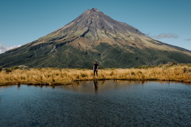 Jeune homme debout près de la haute montagne et d'un lac, parc national d'Egmont au nord de la Nouvelle-Zélande