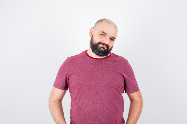 Jeune homme debout tout droit et se présentant à la caméra en t-shirt rose et l'air optimiste, vue de face.