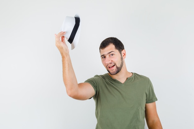 Jeune homme décollant chapeau en t-shirt vert et chapeau et à la recherche de beau