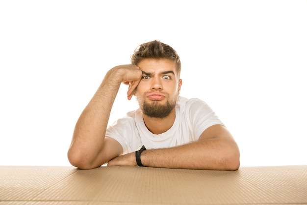 Jeune homme déçu ouvrant le plus gros colis postal isolé sur blanc. Modèle masculin choqué sur le dessus de la boîte en carton regardant à l'intérieur.