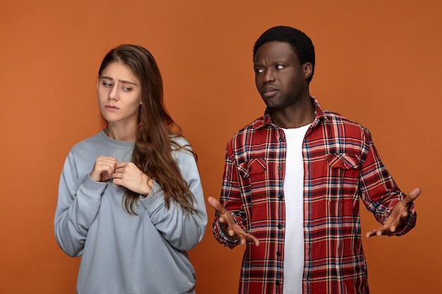 Un jeune homme désemparé d'origine africaine étant perdu, regardant sa petite amie avec une expression faciale confuse, ne peut pas du tout la comprendre. Femme blanche incertaine se sentant mécontente de son petit ami