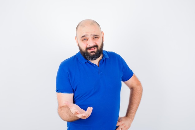 Jeune homme discutant de quelque chose tout en montrant des gestes de la main en chemise bleue et en ayant l'air concentré. vue de face.