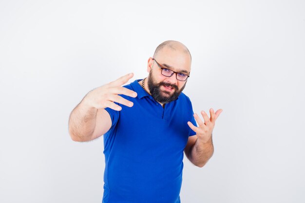 Jeune homme discutant tout en montrant des gestes de la main en chemise bleue, lunettes et semblant bavard. vue de face.
