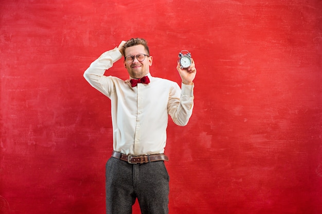 Le jeune homme drôle avec horloge abstraite sur fond de studio rouge. concept - temps de féliciter