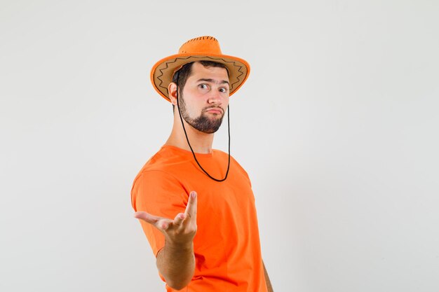 Jeune homme écartant la main de manière perplexe en t-shirt orange, vue de face du chapeau.