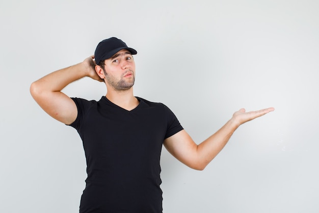 Jeune homme écartant la paume de côté avec la main derrière la tête en t-shirt noir