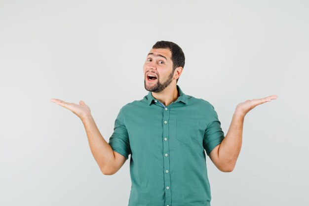 Jeune homme écartant la paume pour montrer quelque chose en chemise verte et avoir l'air joyeux. vue de face.