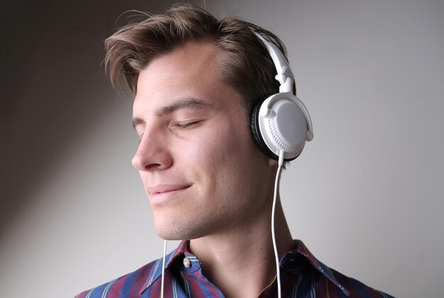 Jeune homme écoutant de la musique avec des écouteurs contre un mur gris