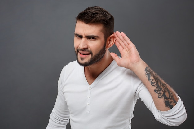 Jeune homme, écoute, tenant main, près, oreille, sur, mur gris