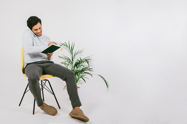 Photo gratuite jeune homme écrit sur son journal et parle au téléphone