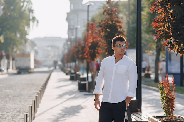 Jeune homme élégant dans une chemise marchant dans une rue européenne par une journée ensoleillée