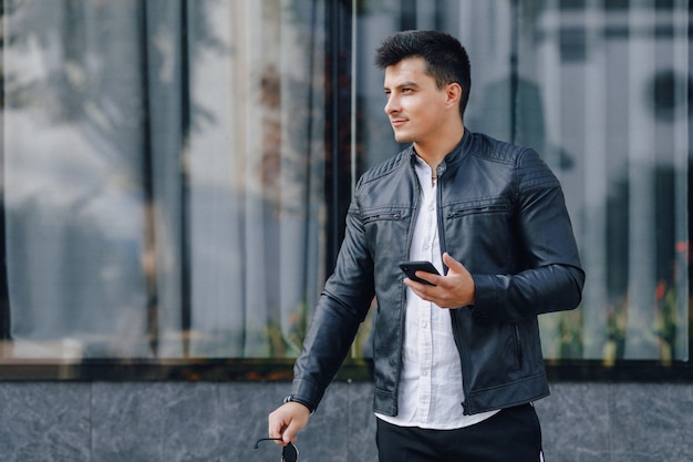 Jeune homme élégant dans des verres en veste de cuir noir avec téléphone