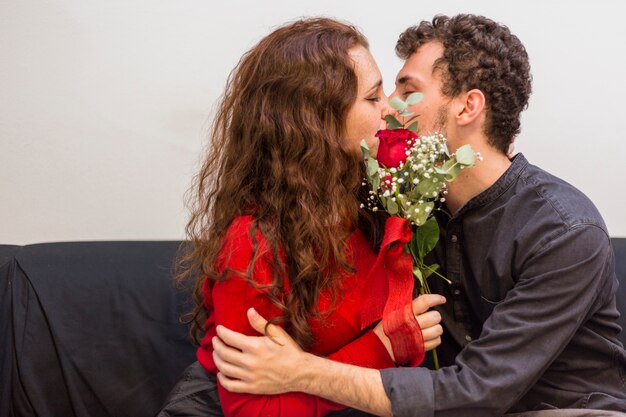 Jeune homme embrasse une femme avec une rose rouge