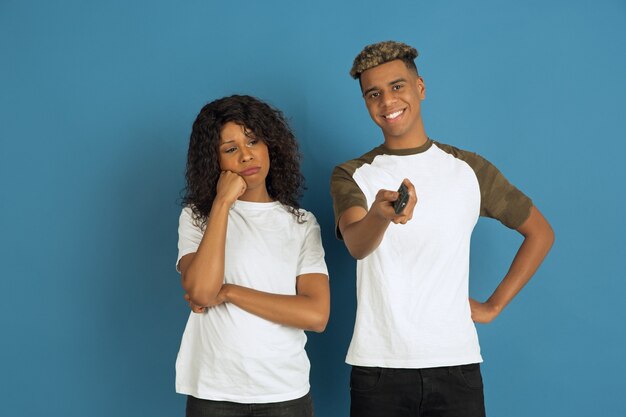 Jeune homme émotionnel et femme en vêtements décontractés blancs posant sur bleu.