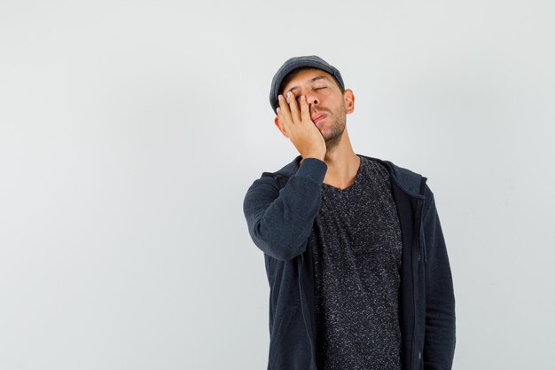 Jeune homme endormi avec la main sur la joue en t-shirt, veste, casquette et à épuisé