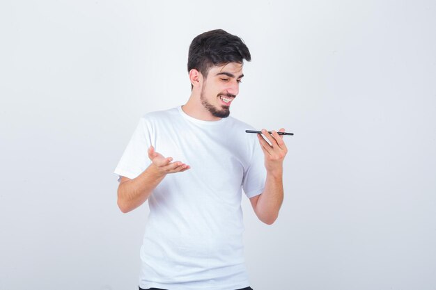 Jeune homme enregistrant un message vocal sur un téléphone portable en t-shirt et ayant l'air heureux